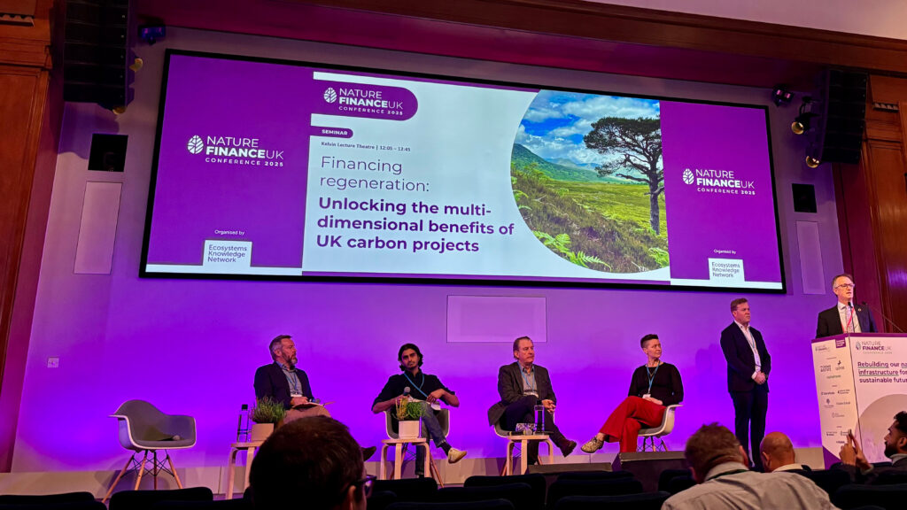 A photo of a stage at a conference with a panel of four people and one speaker.